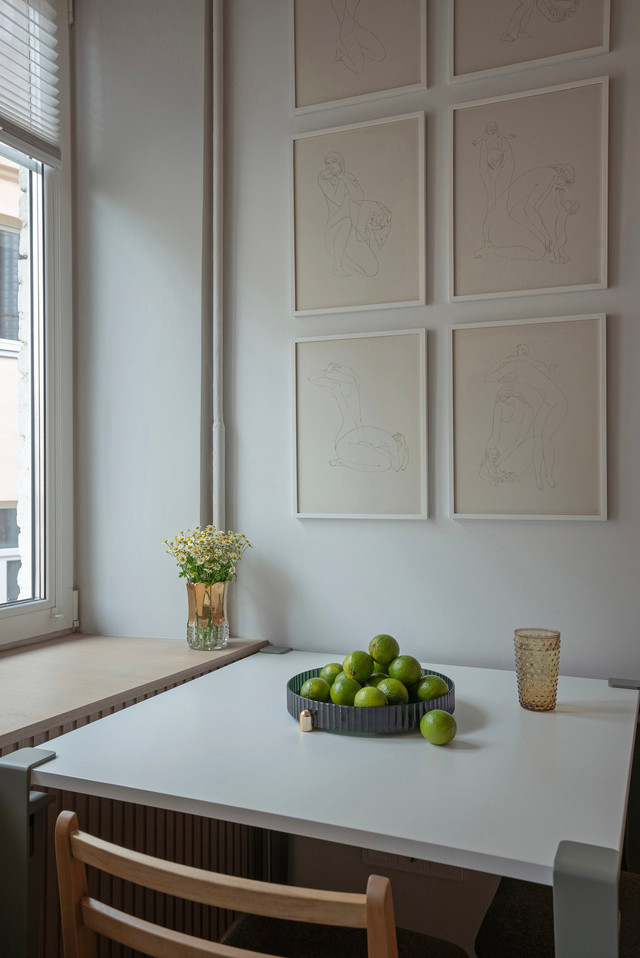 A table with apples stands by the window, and framed drawings hang on the wall.