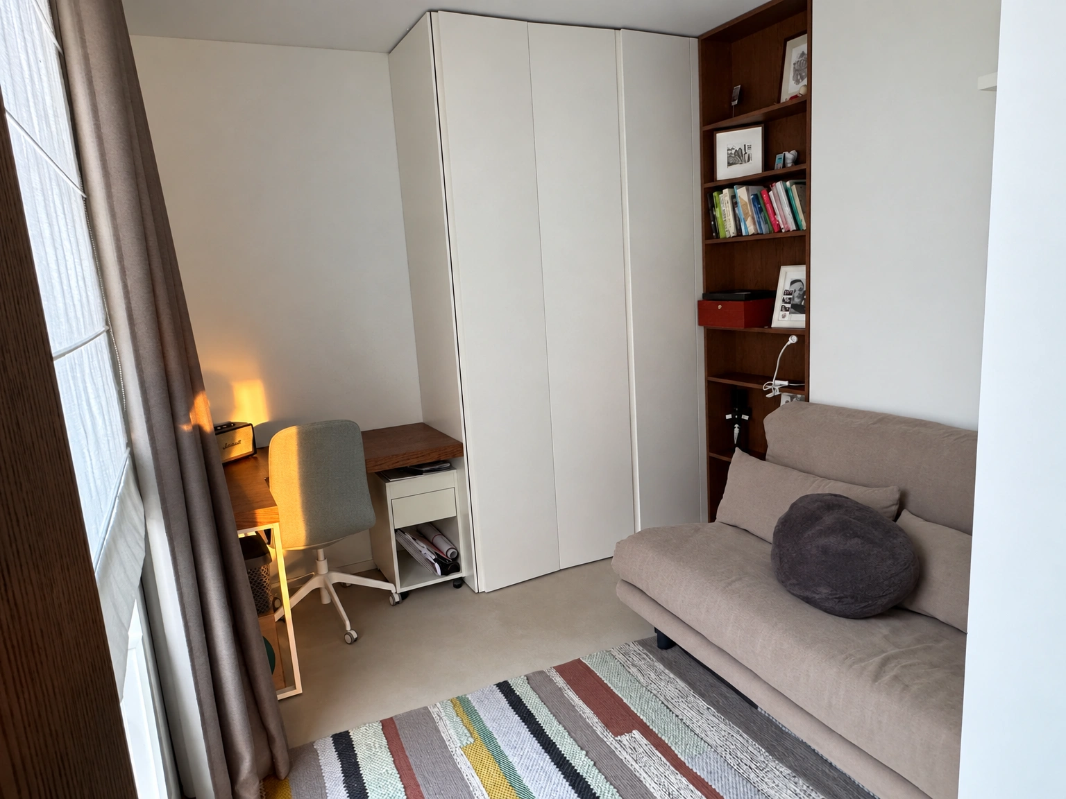 A room with a grey sofa and a desk by the window.