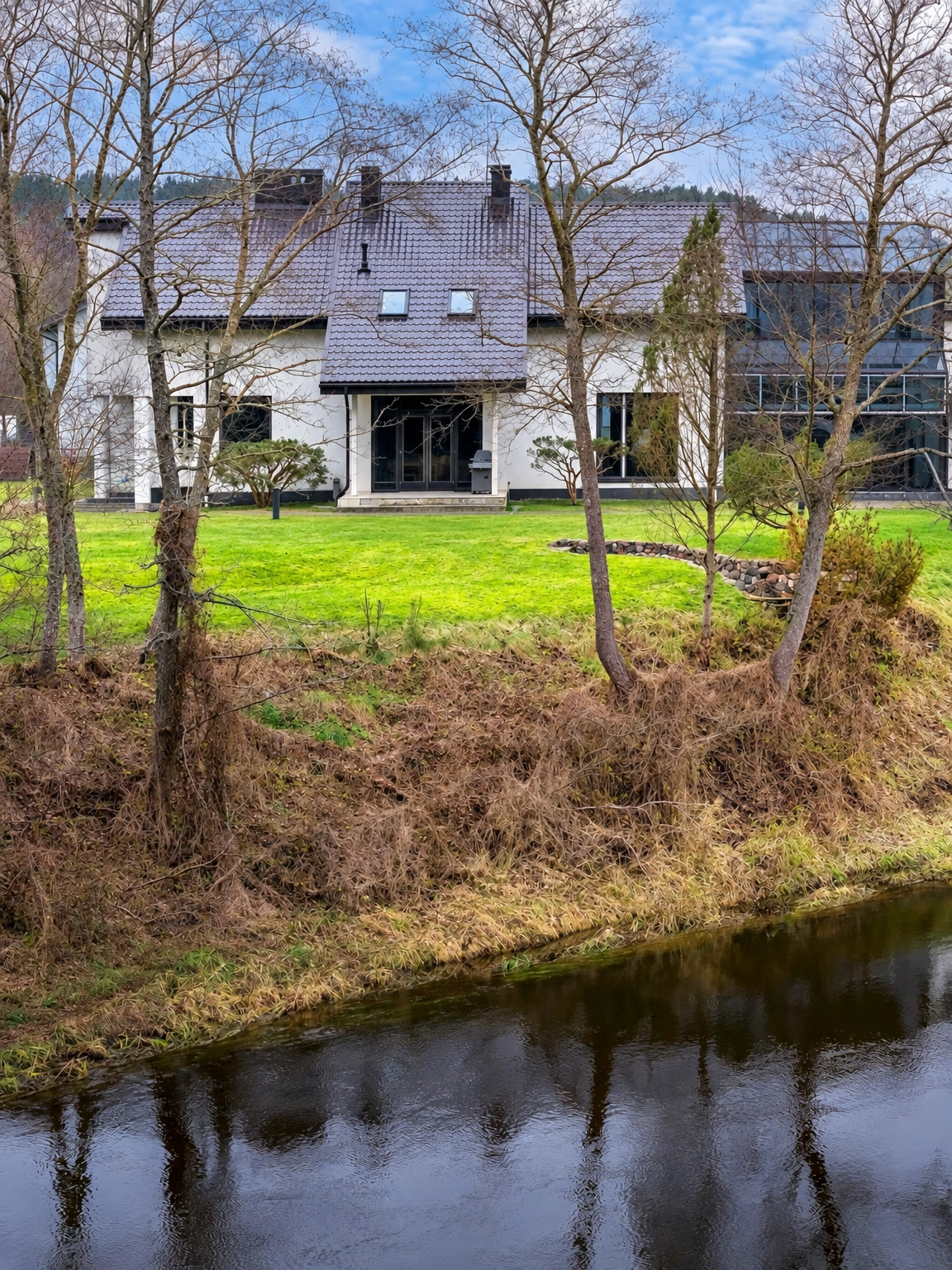 Ein Haus mit großen Fenstern und einem grünen Rasen neben einem Gewässer.