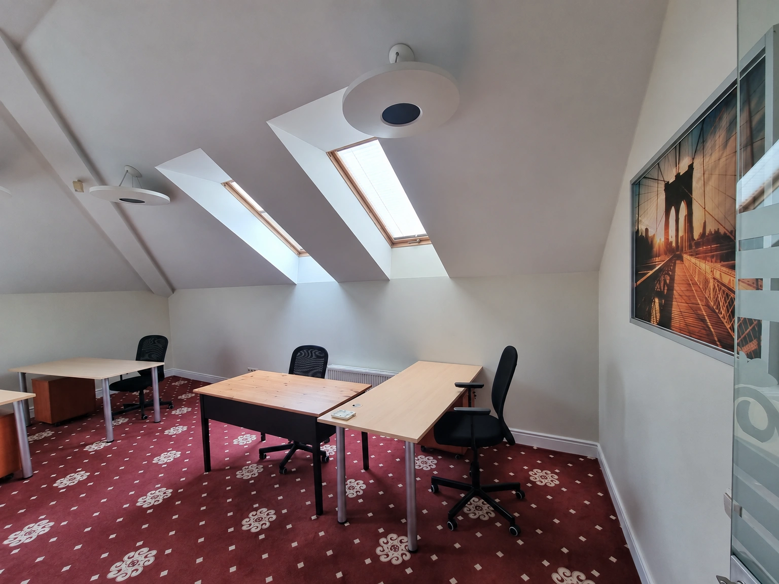 There are tables and office chairs in the attic room, and skylights are installed in the sloping ceiling.