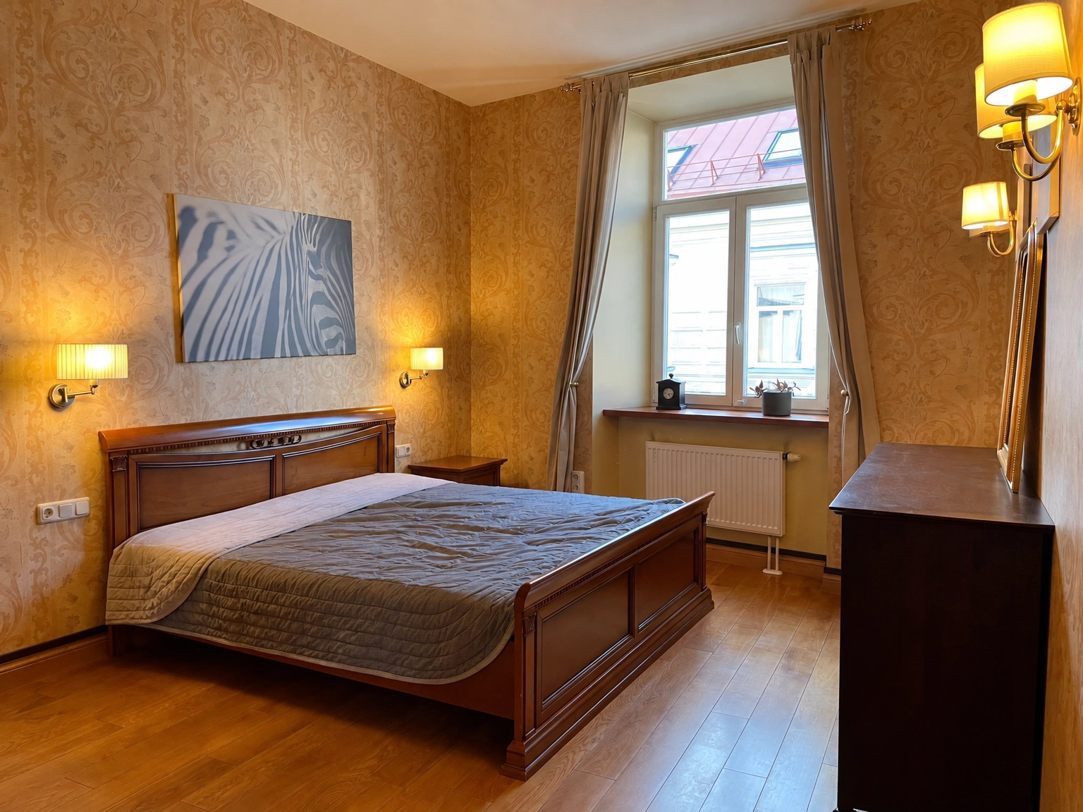 Im Schlafzimmer stehen ein Doppelbett und eine Kommode, am Fenster hängen Vorhänge.
