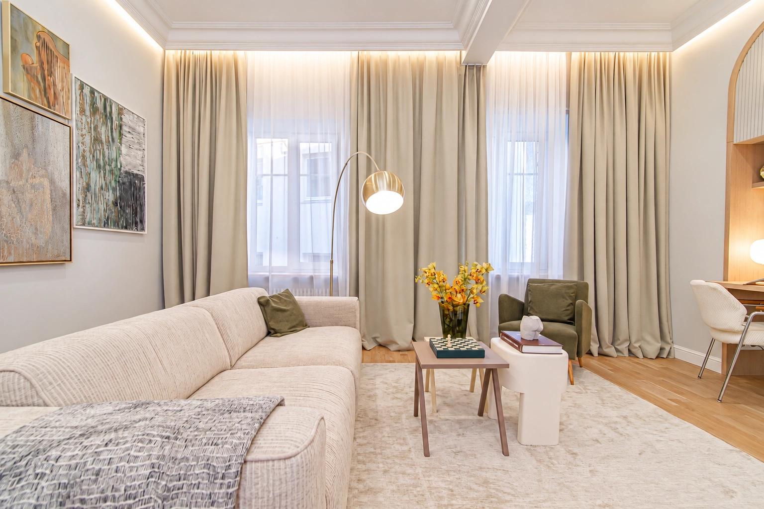 A living room with a light-colored sofa, two small tables, and long curtains by the windows.