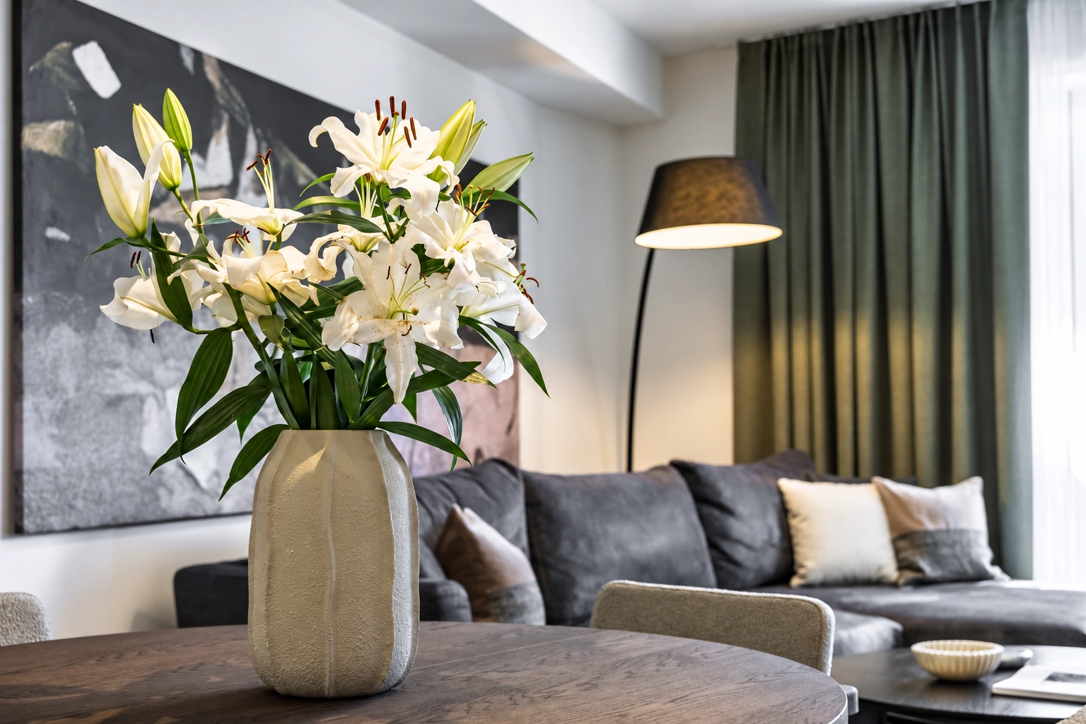 Im Wohnzimmer steht ein graues Sofa, und auf dem Tisch steht eine Vase mit weißen Blumen.