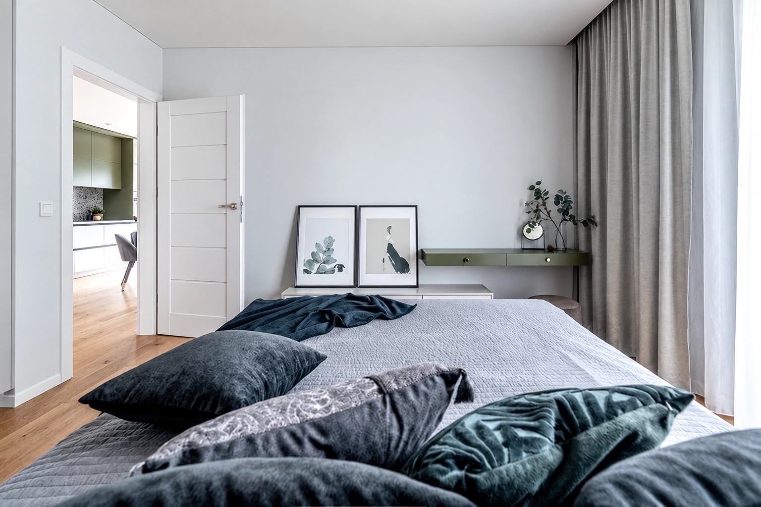 Im Schlafzimmer steht ein Bett mit dunklen Kissen, und am Fenster hängen graue Vorhänge.