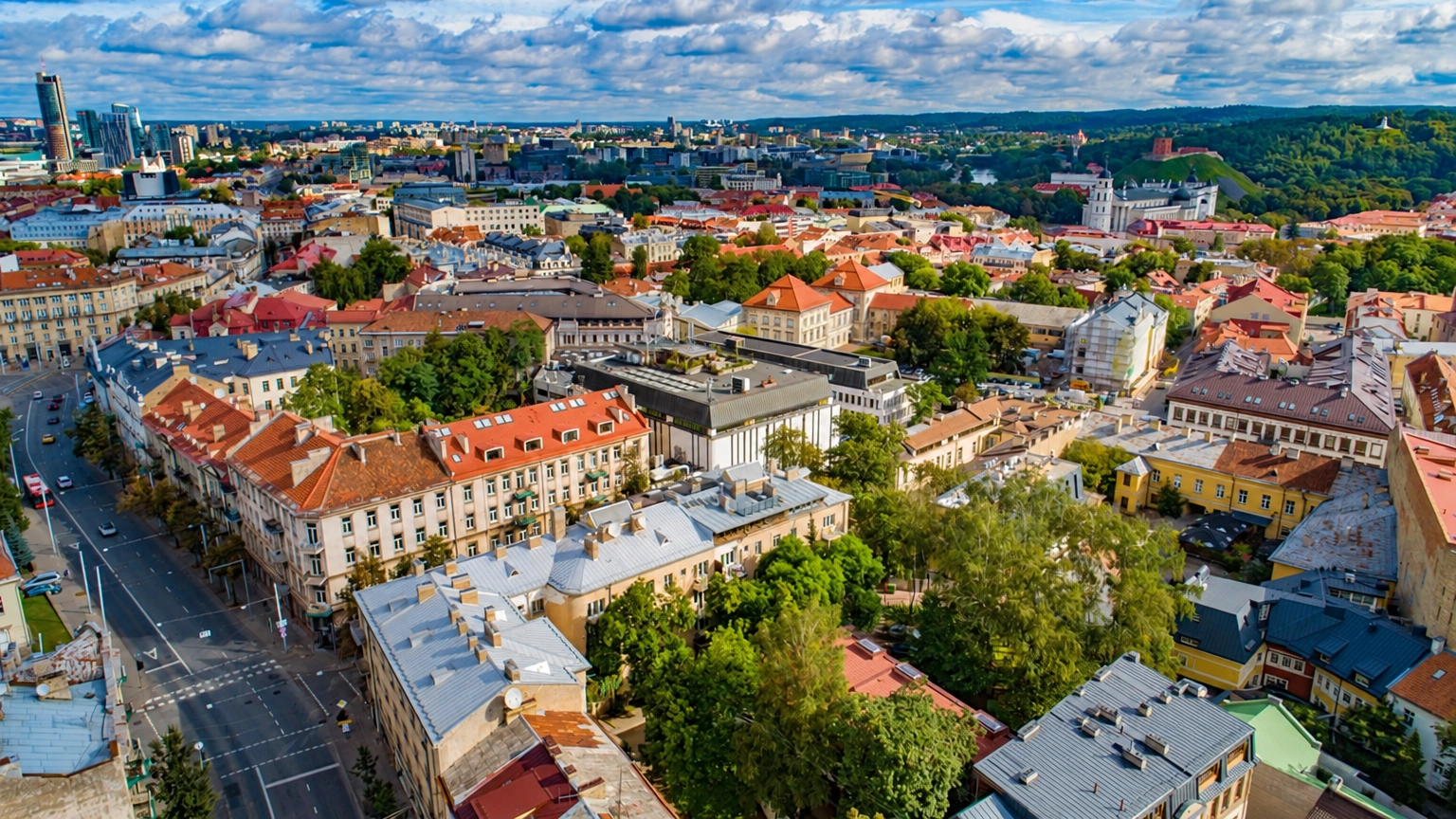 Miesto panorama iš viršaus su raudonais stogais ir tarp pastatų augančiais medžiais.