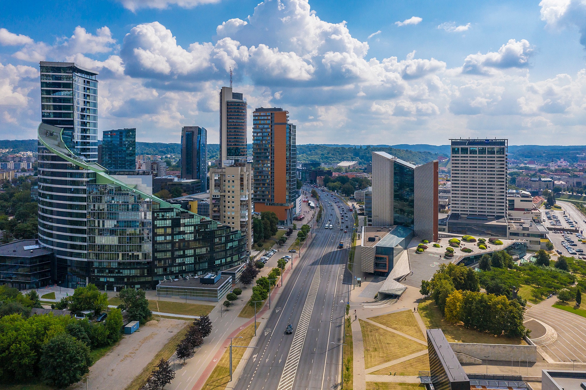 City view with a wide street, multi-storey buildings and trees.
