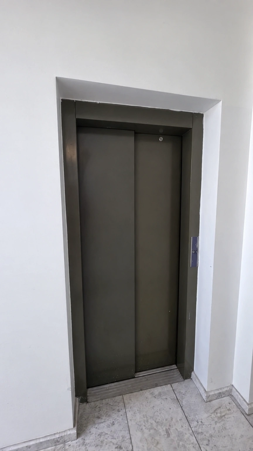 Dark elevator doors, white walls and a light-colored floor are visible in the corridor.