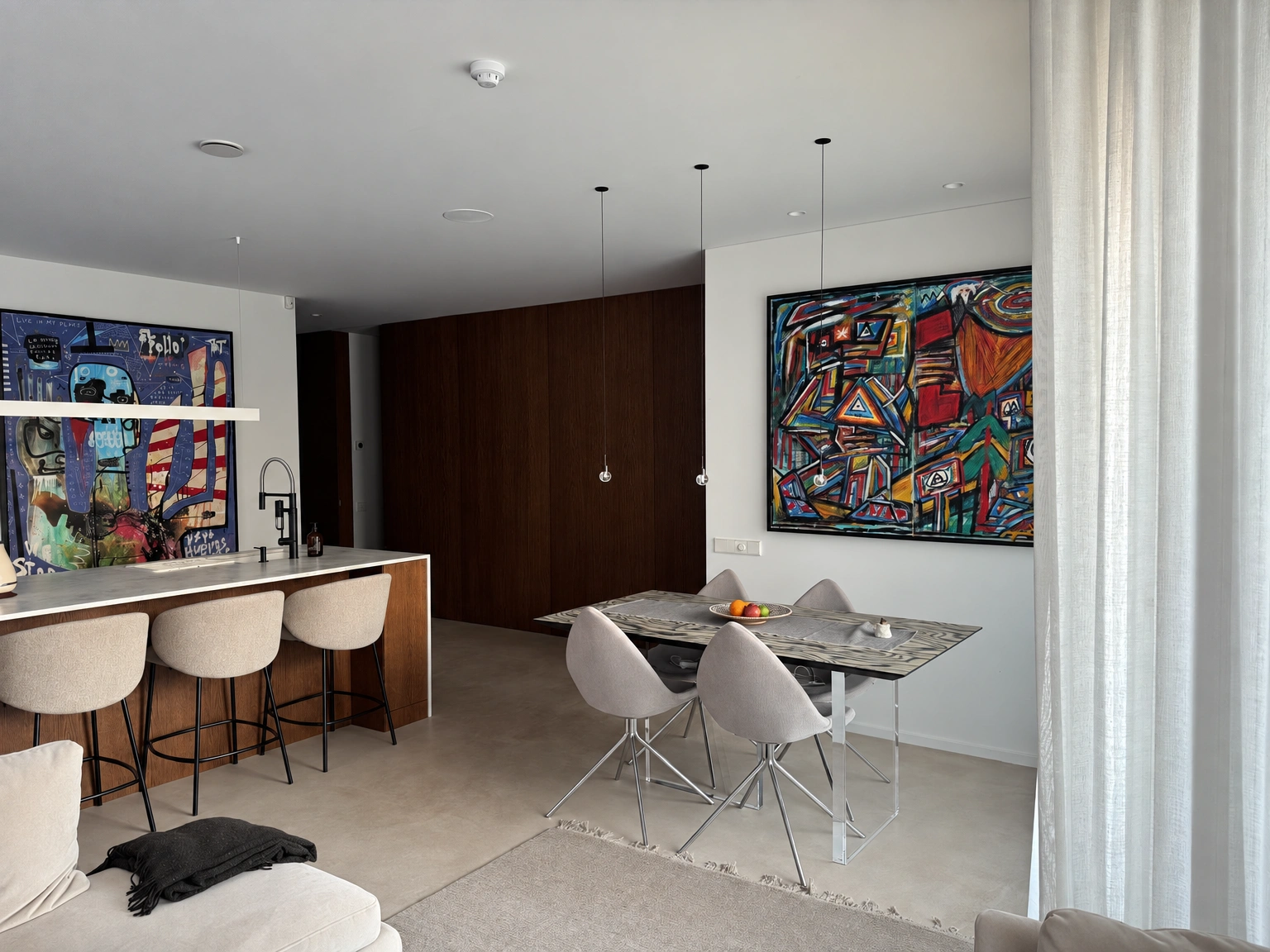 Dining area with a table and light-colored chairs; a colorful painting hangs on the wall.