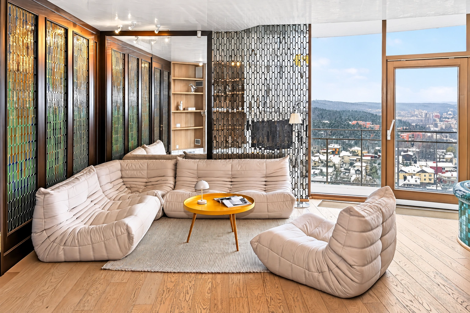 Wohnzimmer mit Polstermöbeln und großen Fenstern, durch die die Stadt zu sehen ist.