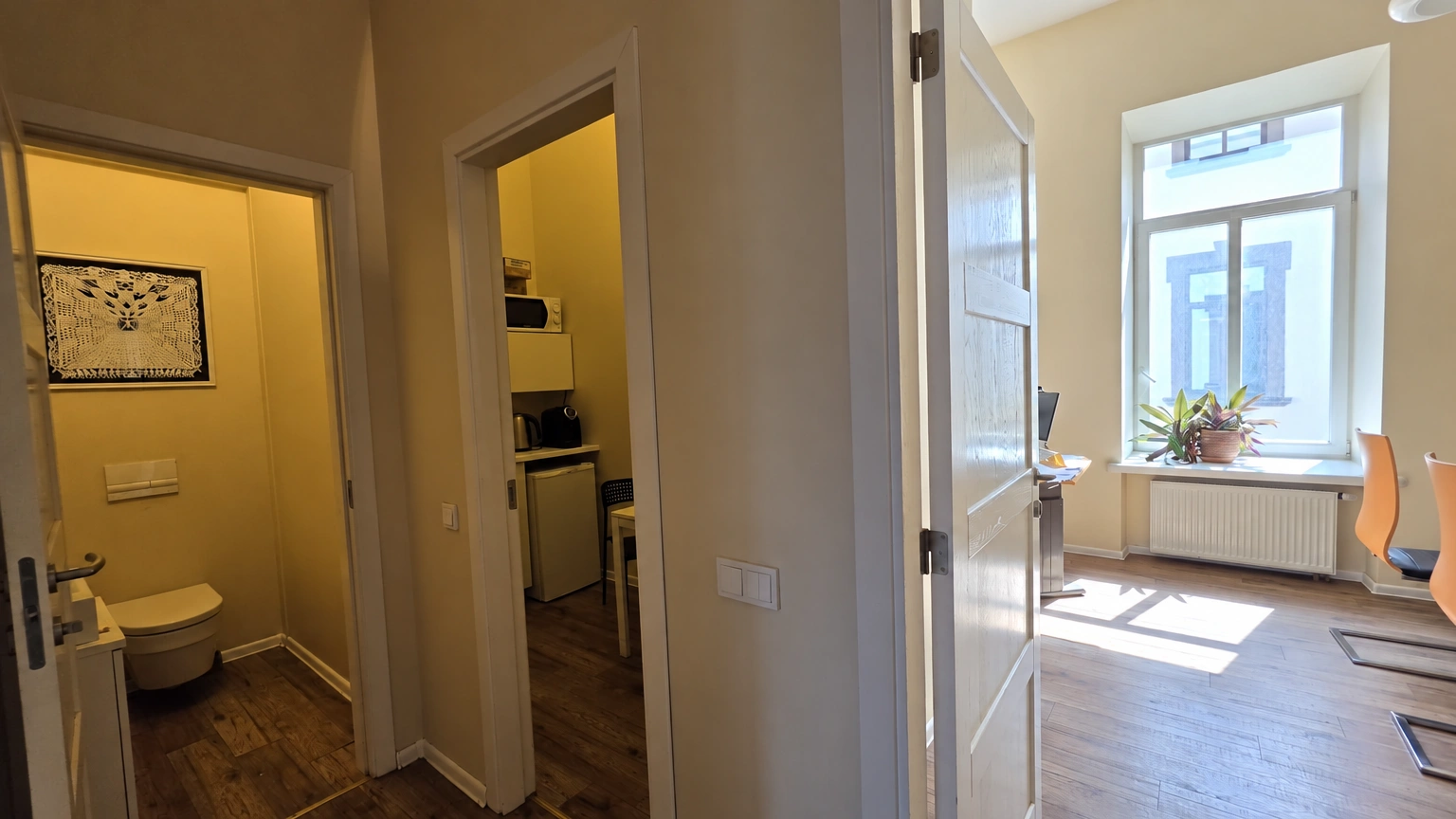 A corridor with open doors leading to several rooms; a window and a radiator are visible on the right.