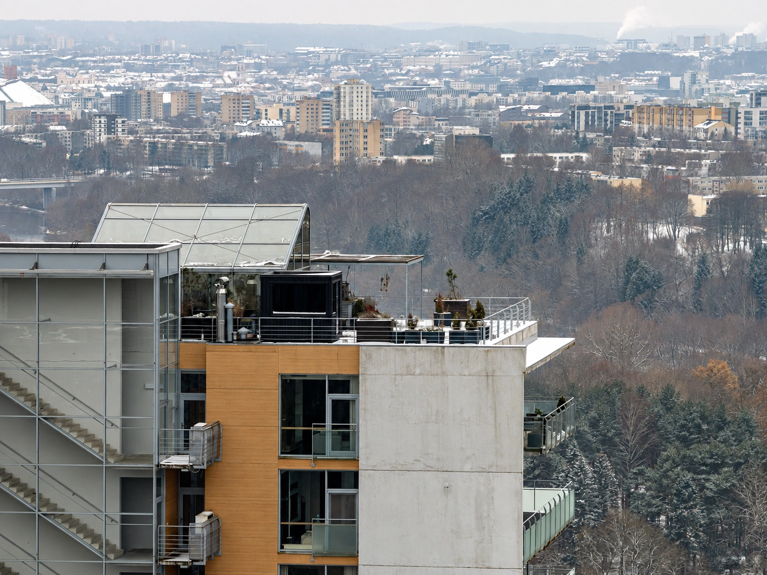 Die oberen Stockwerke des Gebäudes und die Dachterrasse, in der Ferne sind Bäume und das Stadtpanorama zu sehen.