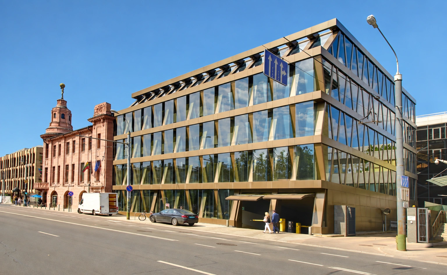 An der Straße steht ein mehrstöckiges Gebäude mit großen Fenstern und diagonalen Fassadenstützen.