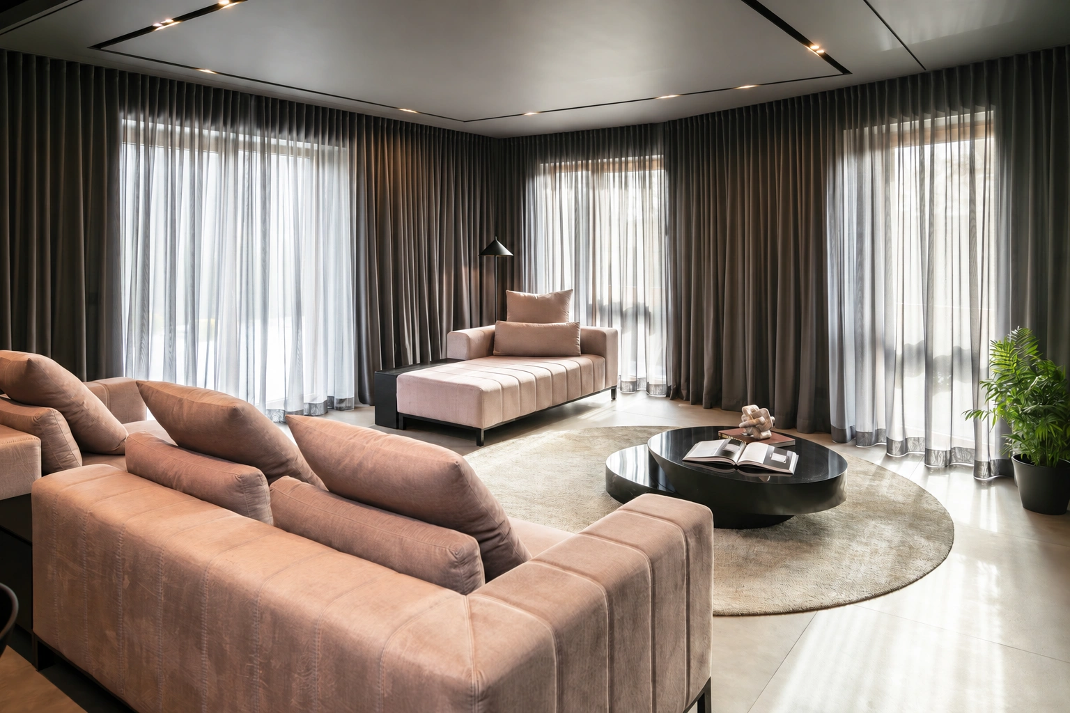 Svetainėje stovi sofa ir apvalus kavos staliukas, o didelius langus dengia užuolaidos.