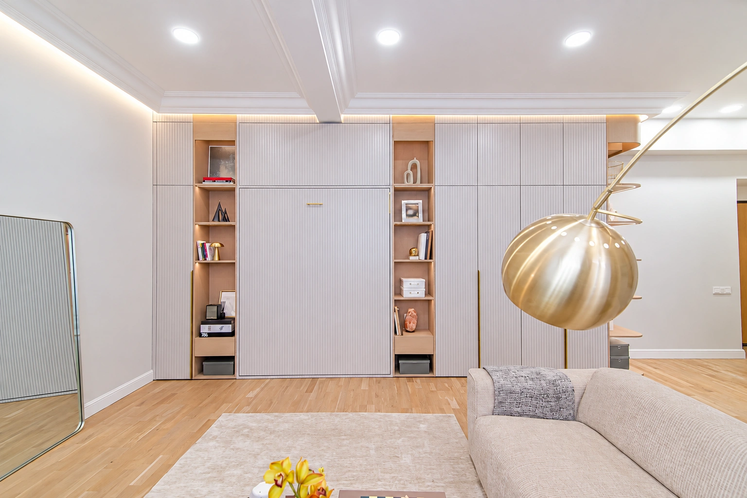 A light-colored sofa, a round light fixture and wall cabinets with open shelves can be seen in the living room.