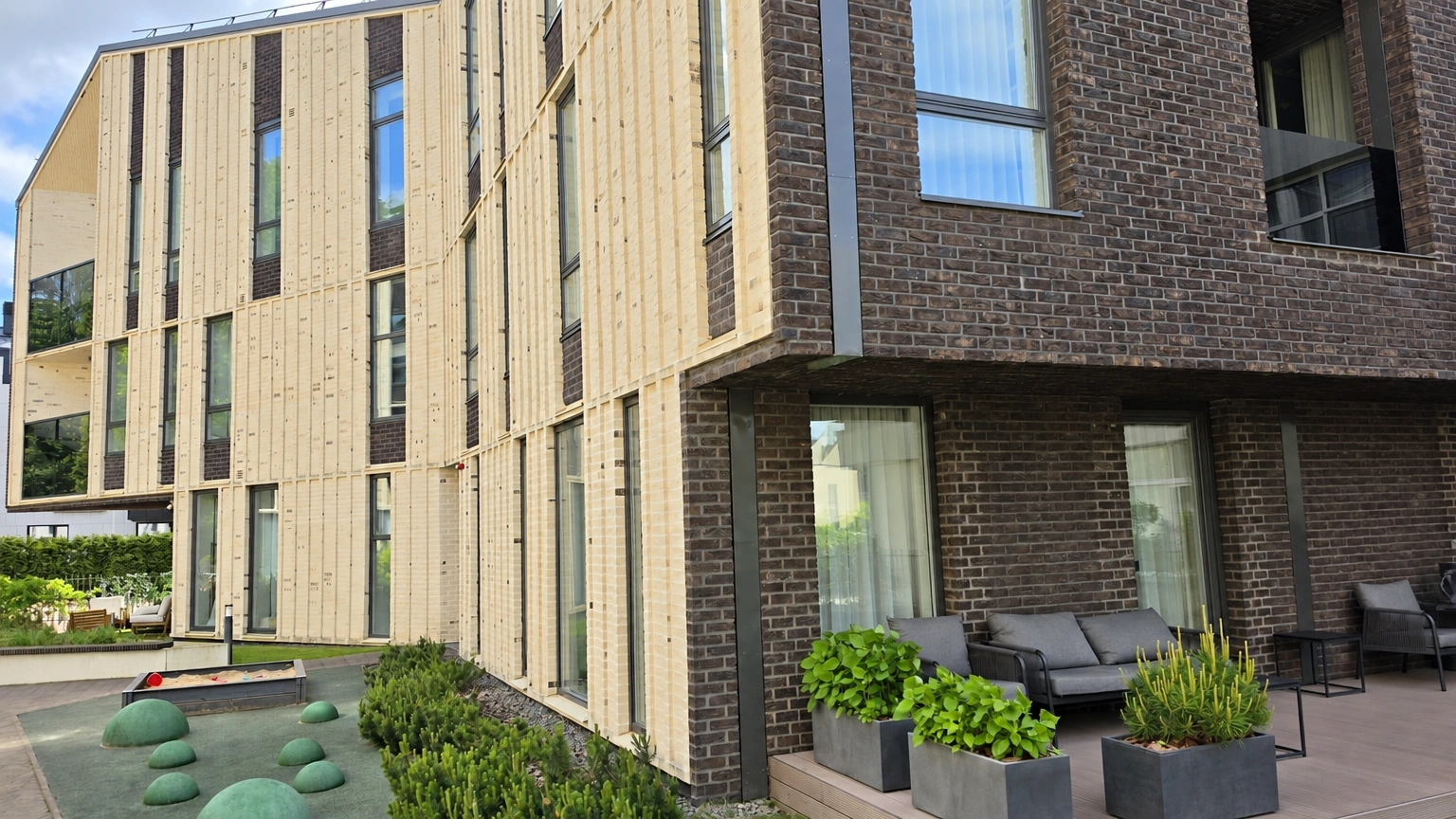 A terrace with outdoor furniture and plant pots has been set up next to a building with large windows.