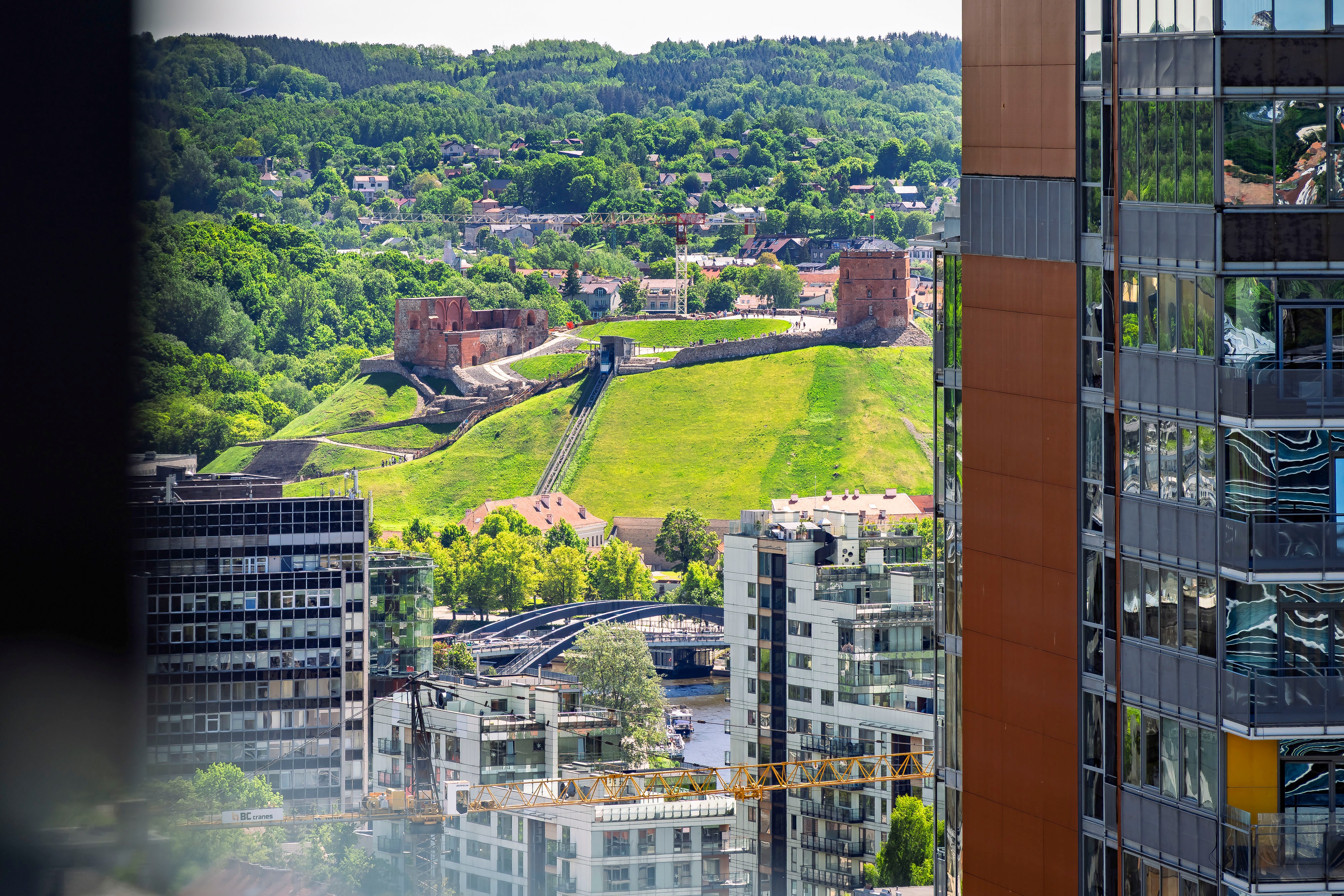 City view with multi-storey buildings and a green hill surrounded by trees.