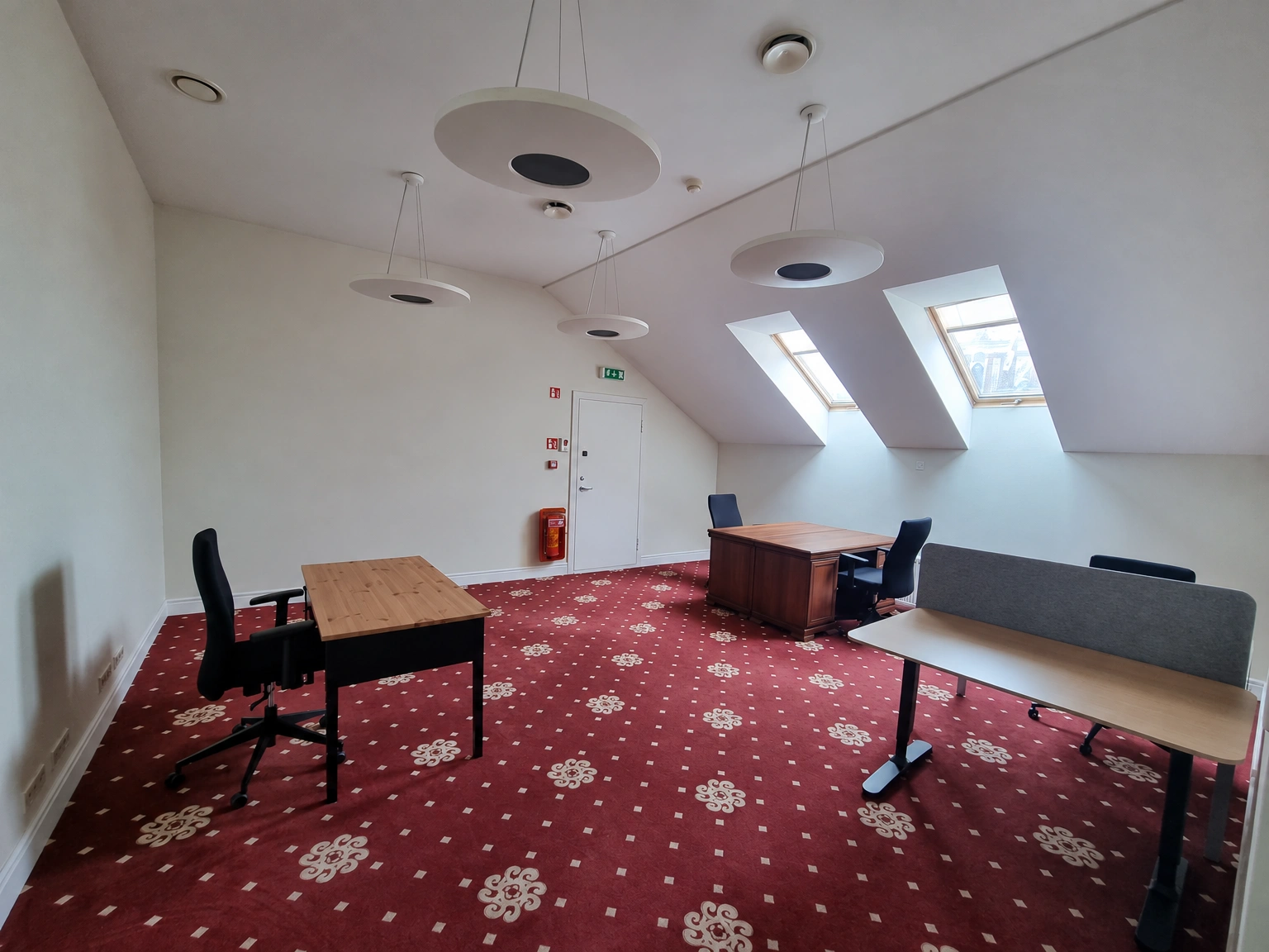 A room with work desks, black chairs, and skylights in the sloped ceiling.