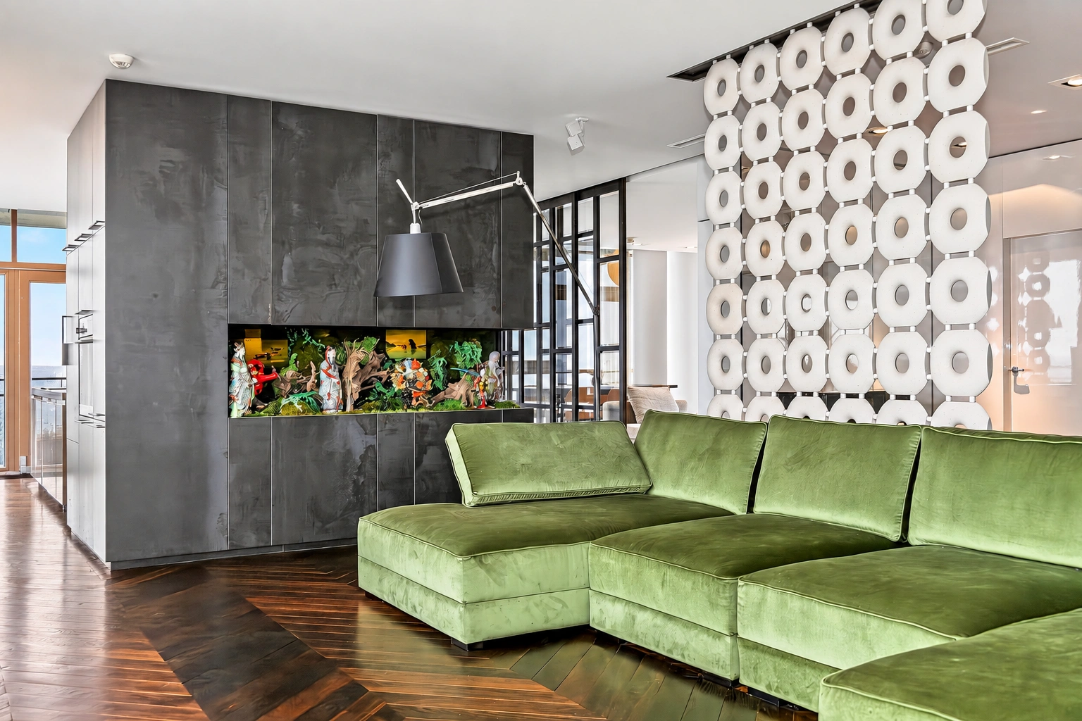Wohnzimmer mit einem grünen Ecksofa und einer weißen durchbrochenen Trennwand.