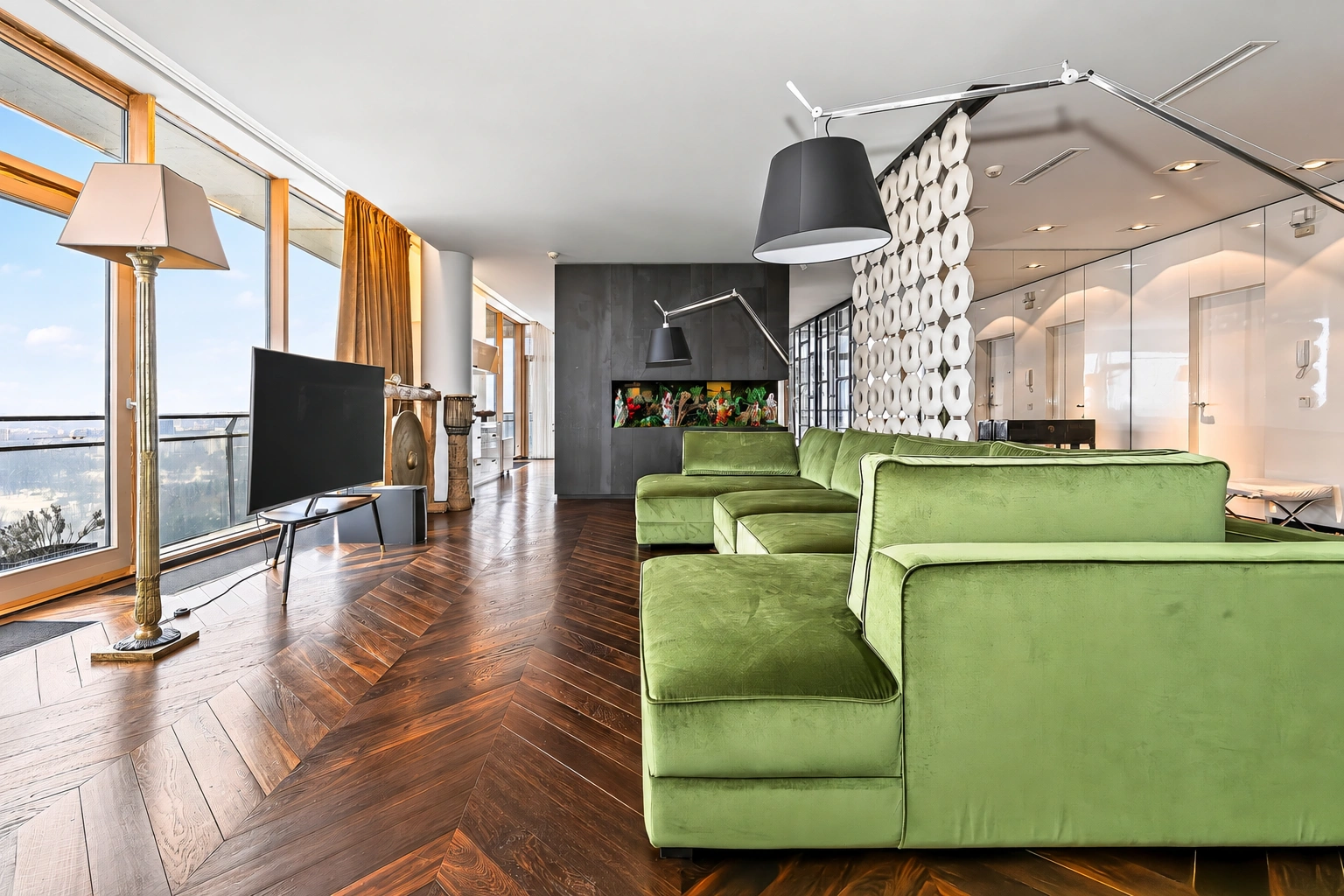 Im Wohnzimmer sind ein grünes Sofa und große Fenster entlang der Wand zu sehen.
