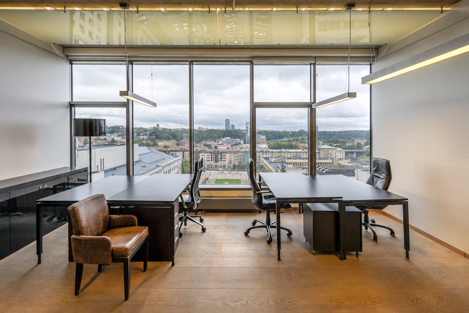 There are two desks and chairs in the office, and the city can be seen through the large windows.