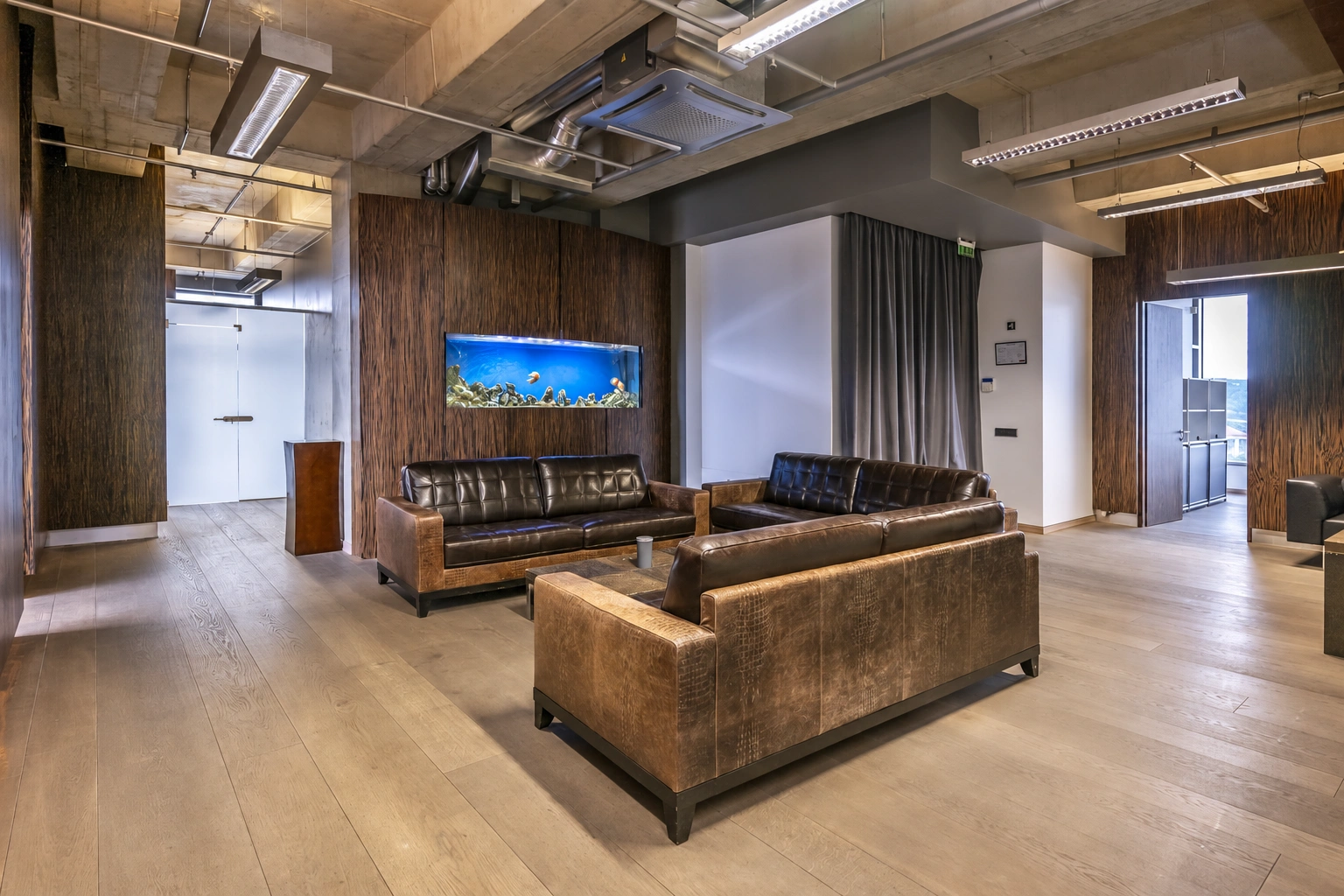 A space with brown sofas, an aquarium built into the wall, and visible ceiling air ducts.