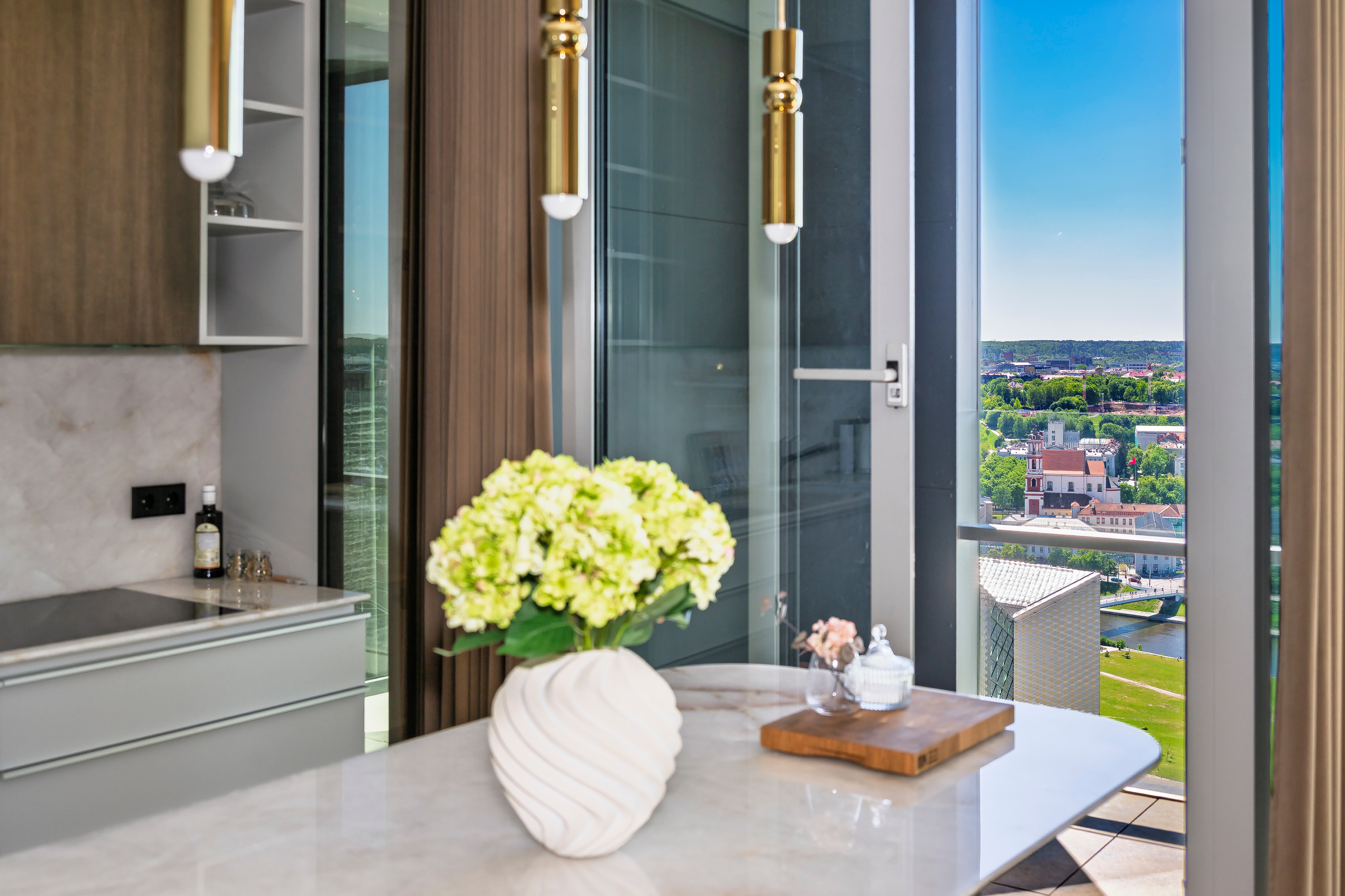 A vase of flowers stands on the countertop, and city buildings can be seen through the window.