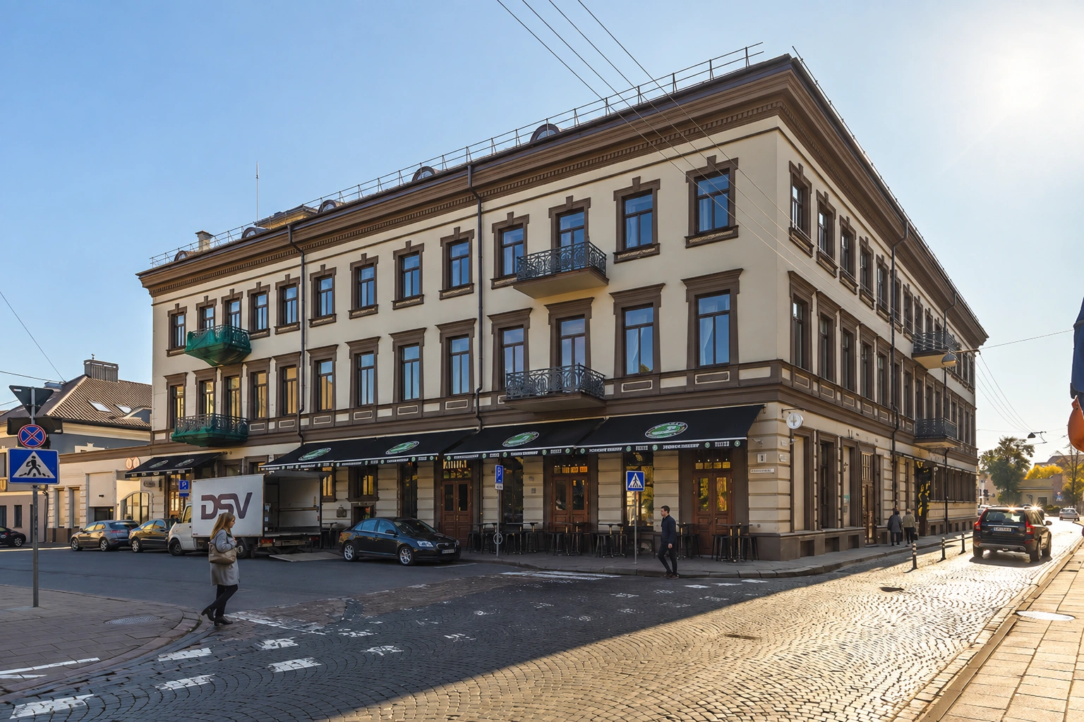 A multi-storey corner building with balconies; next to it is a pedestrian crossing.