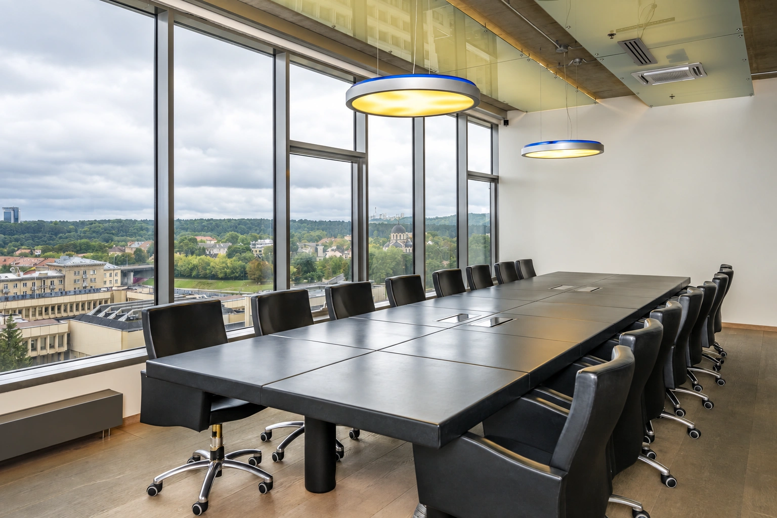 In the meeting room, a long table with black chairs stands near the large windows.