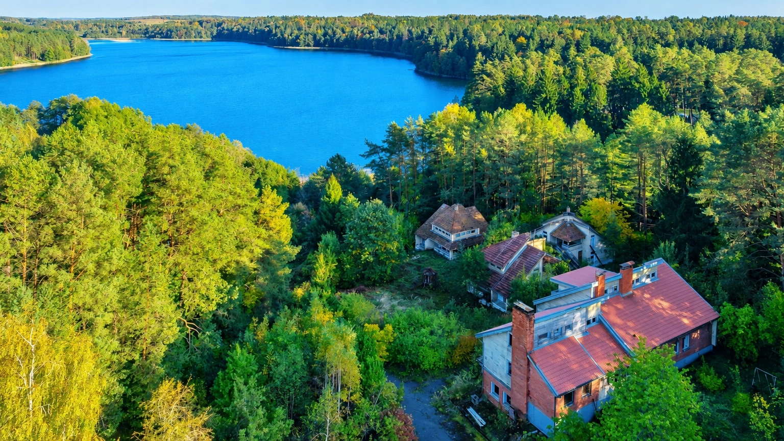 Zwischen den Bäumen steht ein Haus mit einem roten Schrägdach, und in der Ferne ist ein See zu sehen.