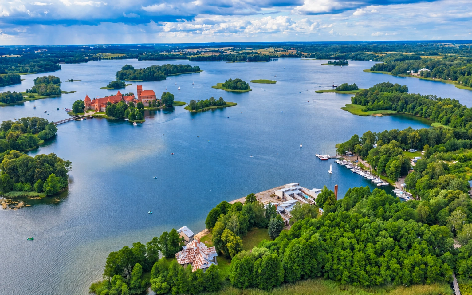 Ežero panorama su miškingomis salomis ir vienoje jų stovinčia pilimi raudonais stogais.