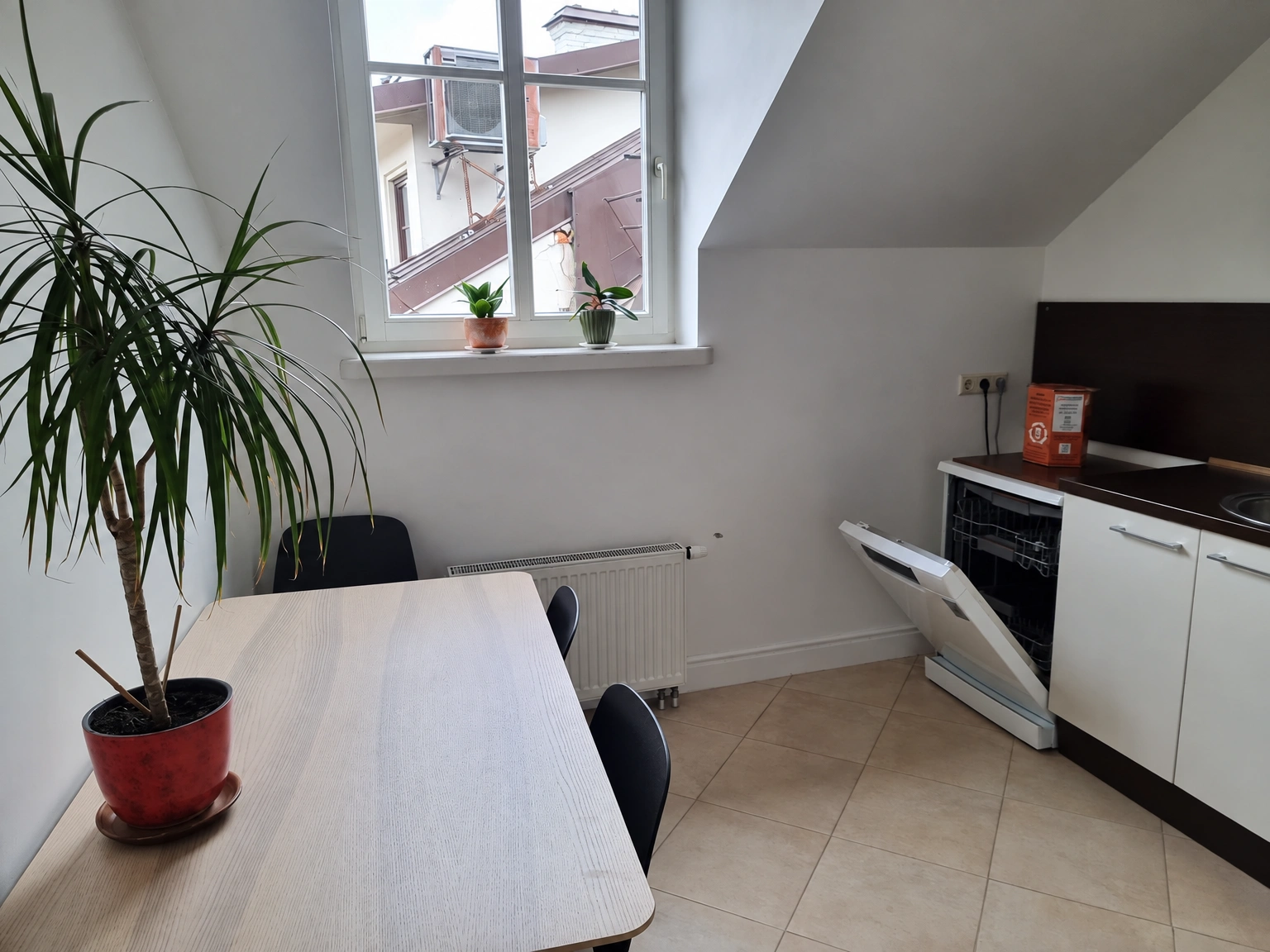 A kitchen with sloped ceilings, white cabinets, and a table by the window.