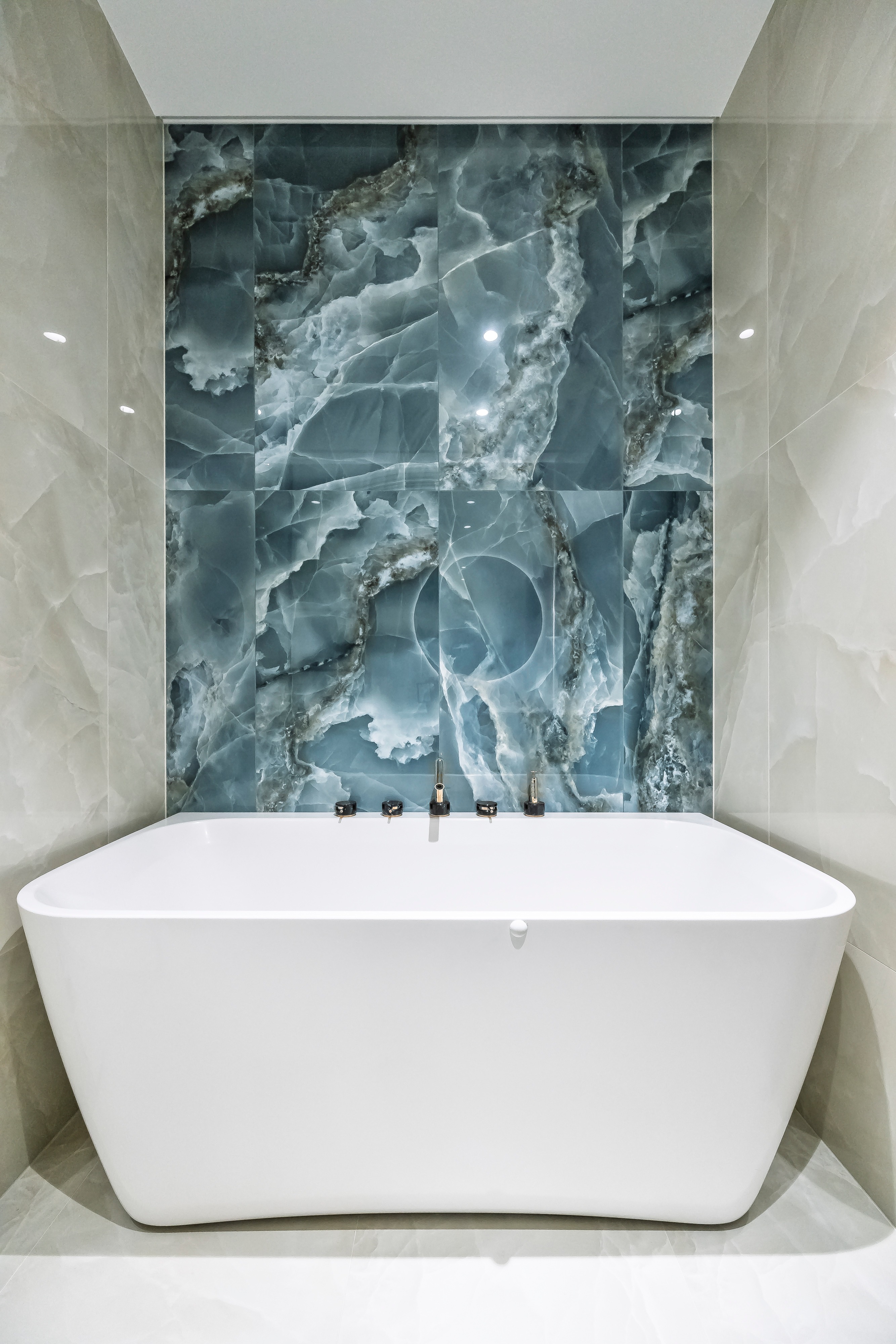 A white freestanding bathtub stands in a niche next to a blue-green patterned wall.