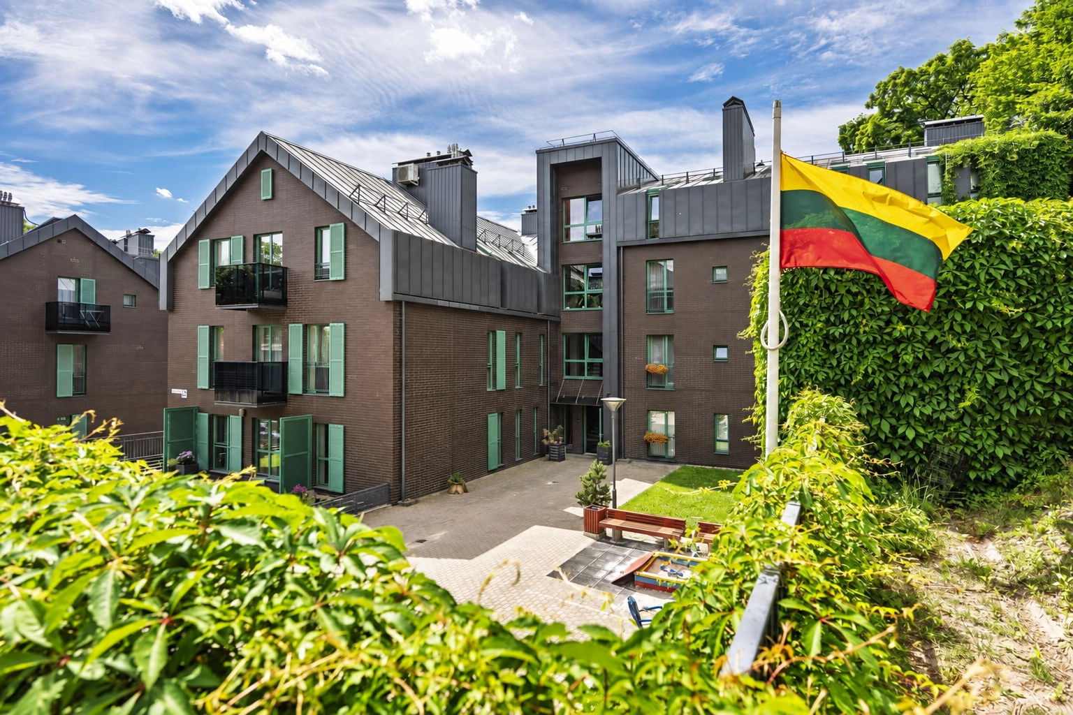 Begrünter Hof eines Mehrfamilienhauses mit einer Bank und einer gehissten litauischen Flagge.