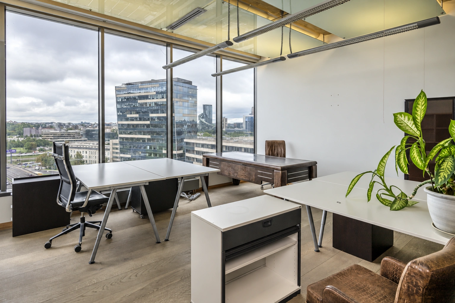 Office space with desks and large windows through which city buildings can be seen.