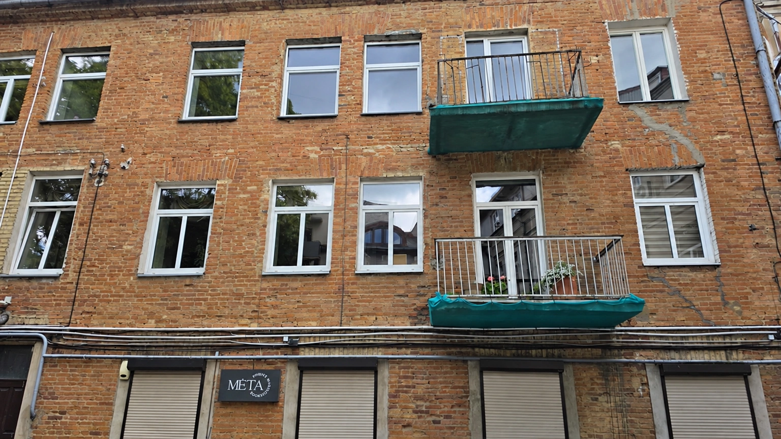 Pastato fasadas su dviem balkonais ir keliomis langų eilėmis.