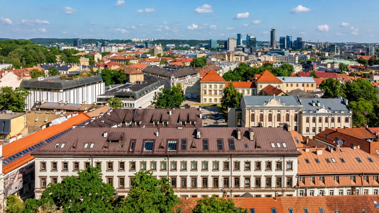 Stadtpanorama mit roten Gebäudedächern und mehrstöckigen Gebäuden, die in der Ferne zu sehen sind.