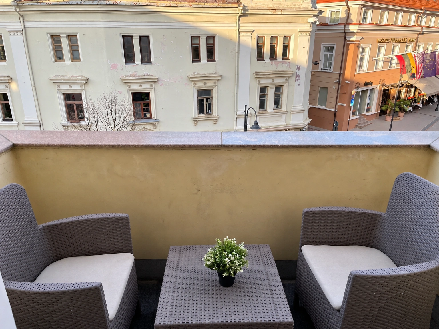 Auf dem Balkon stehen zwei Sessel mit hellen Kissen und ein kleiner Tisch mit einer Topfpflanze.