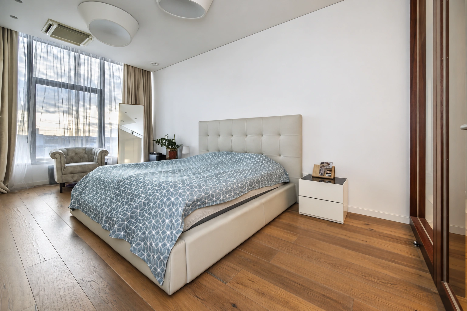 Bedroom with a double bed, a white bedside cabinet and a large window with curtains.