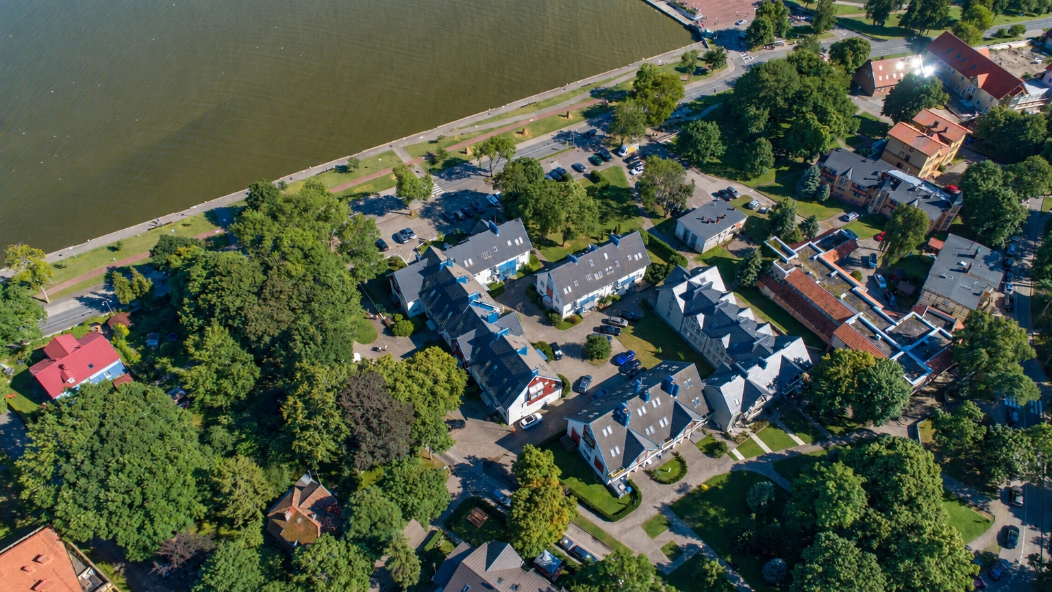 Iš viršaus matomas pastatų kvartalas prie upės, tarp pastatų auga medžiai.