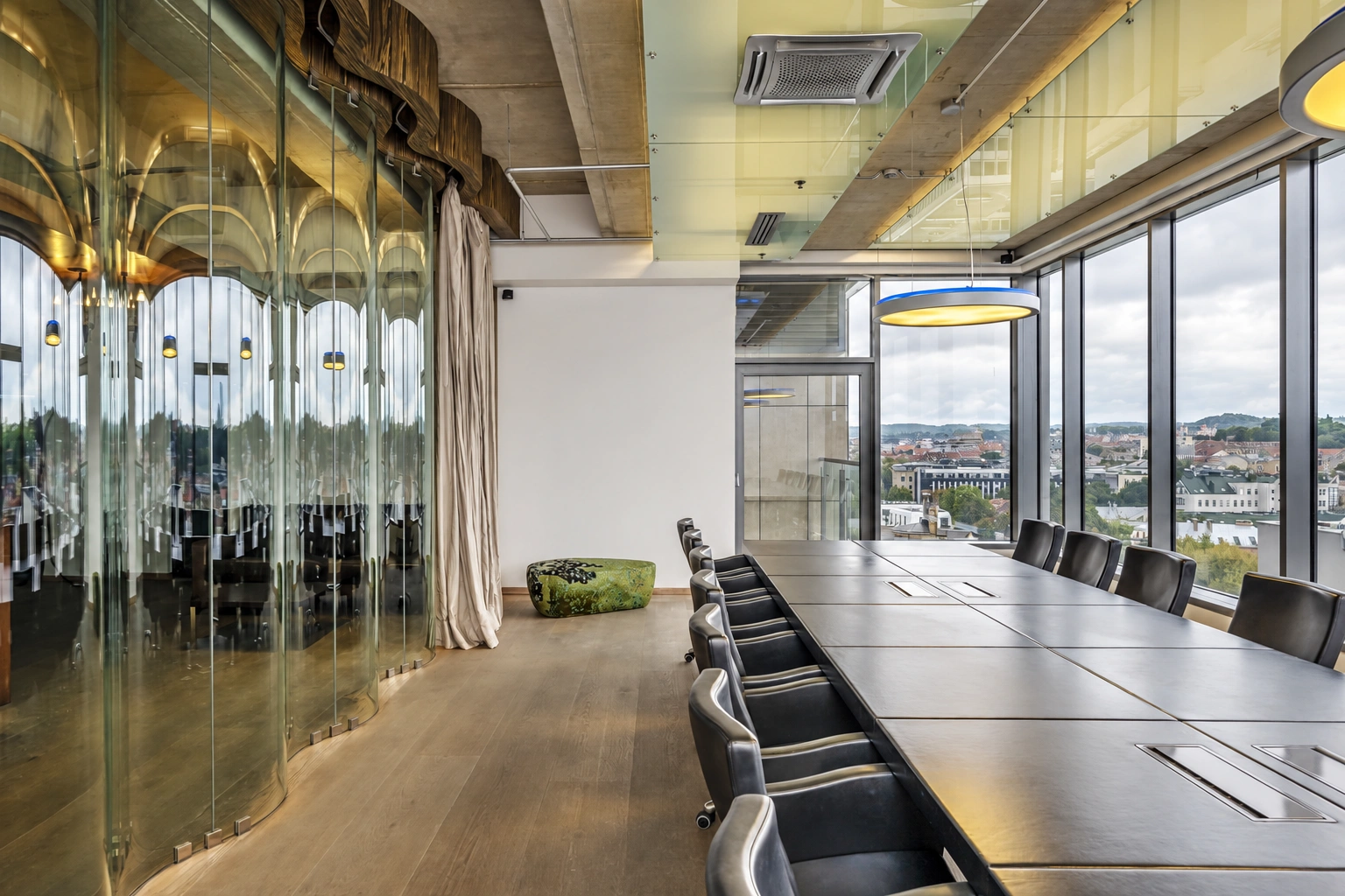 There is a long table with black chairs in the room, and the city is visible through the large windows.