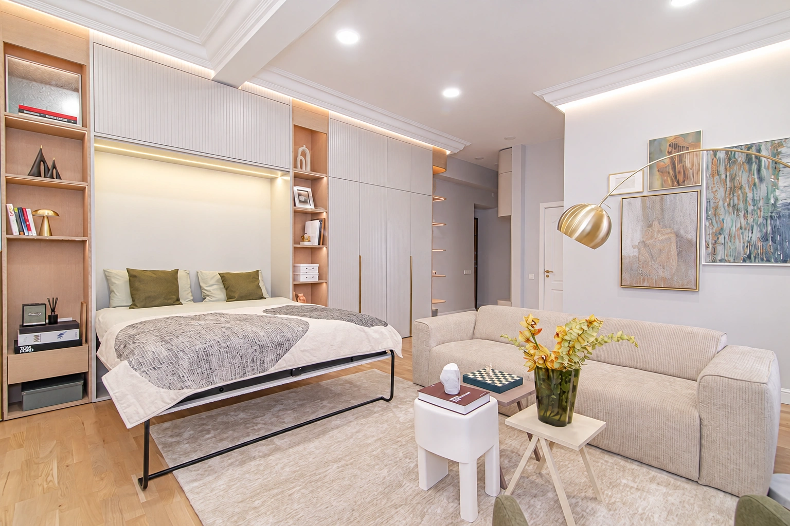 There is a bed and a light-colored sofa in the room, and a vase of yellow flowers on the coffee table.