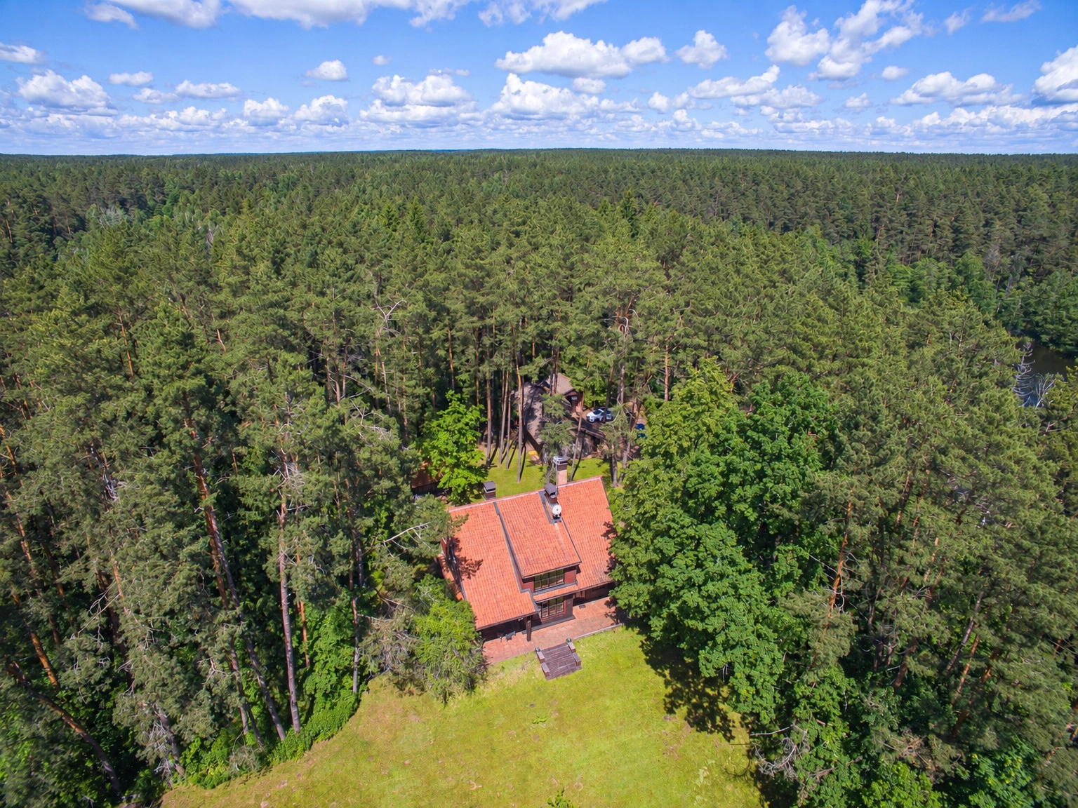 Ein Haus mit einem roten Schrägdach steht umgeben von Wald; daneben ist eine Rasenfläche zu sehen.
