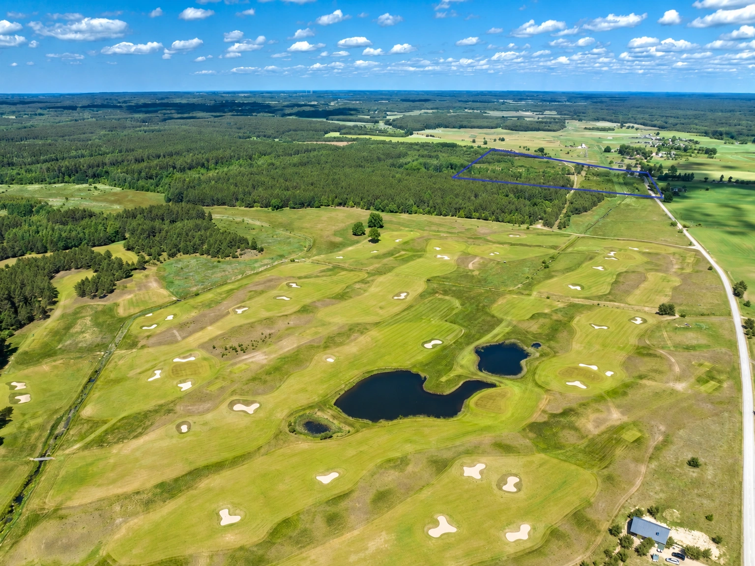 Ein Golfplatz mit Teichen und umliegenden Wäldern, von oben gesehen.