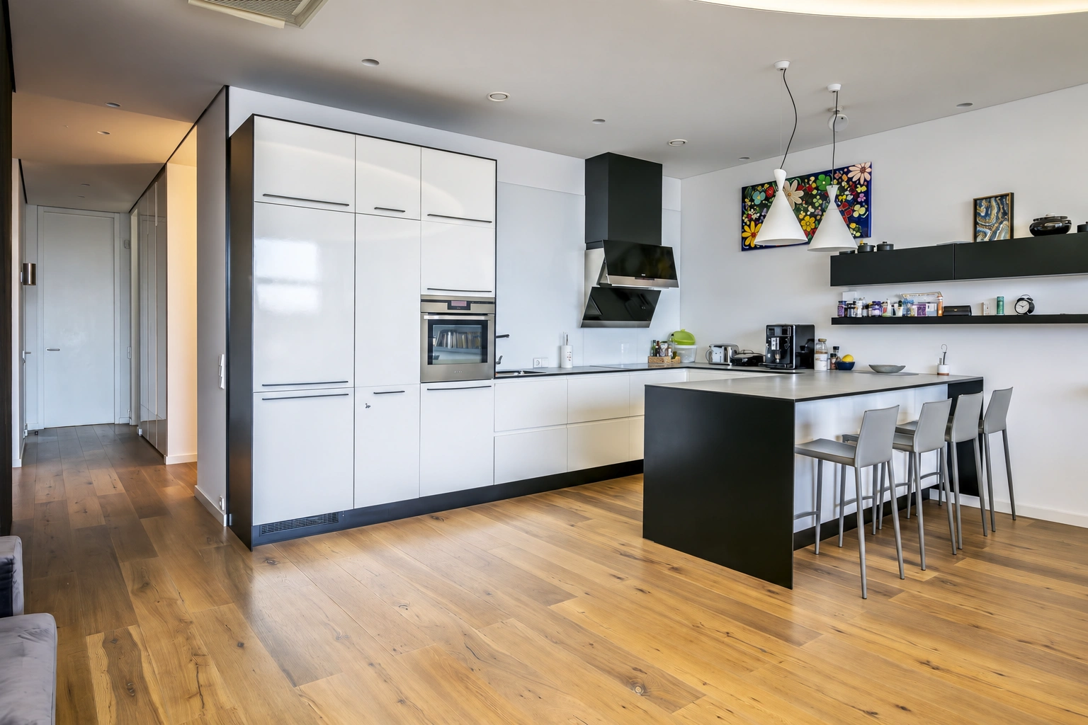 A kitchen with white cabinets and a black island, beside which stand tall chairs.