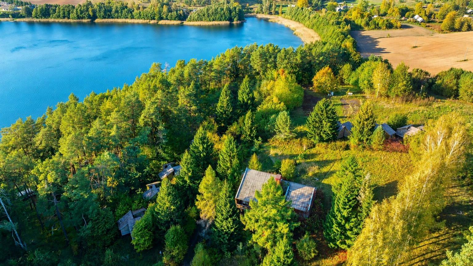 Von oben sind ein See, von Bäumen umgebene Gebäude und eine Wiese zu sehen.
