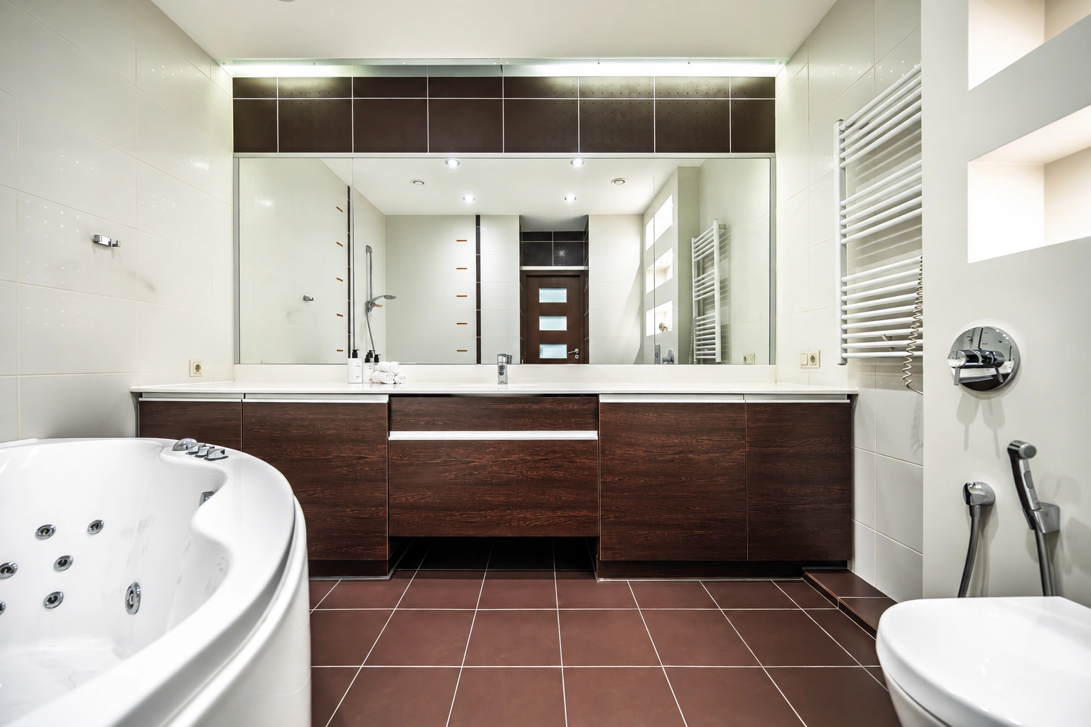 Badezimmer mit einer Whirlpool-Badewanne und einem breiten Spiegel über dem Waschbecken.