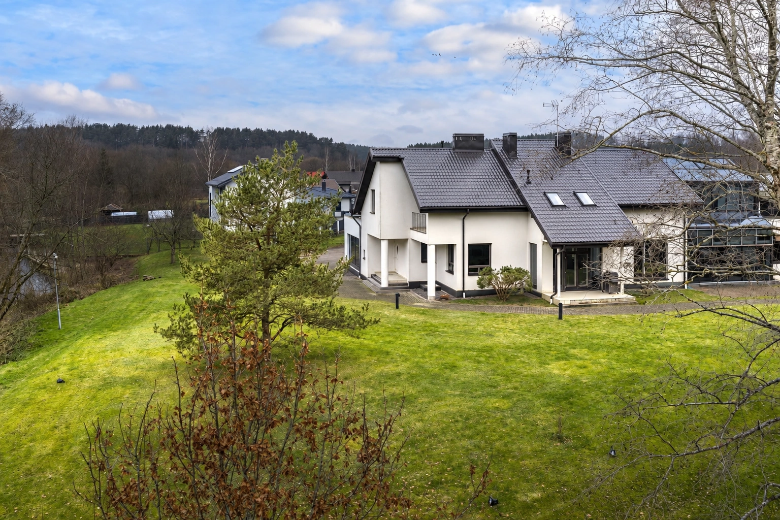 Ein Haus mit einem Schrägdach, vor dem sich eine Rasenfläche erstreckt und Bäume wachsen.