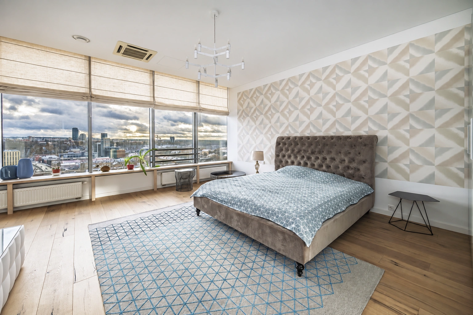A bedroom with a double bed and large windows through which a panoramic view of the city is visible.