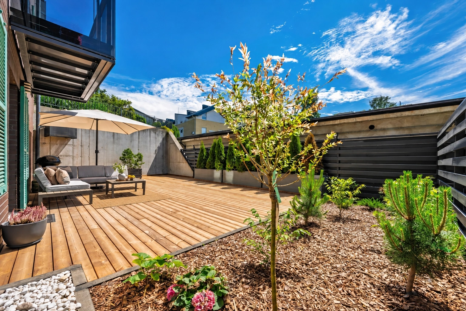 Eine Terrasse mit Gartenmöbeln; daneben wachsen ein Baum und Sträucher.