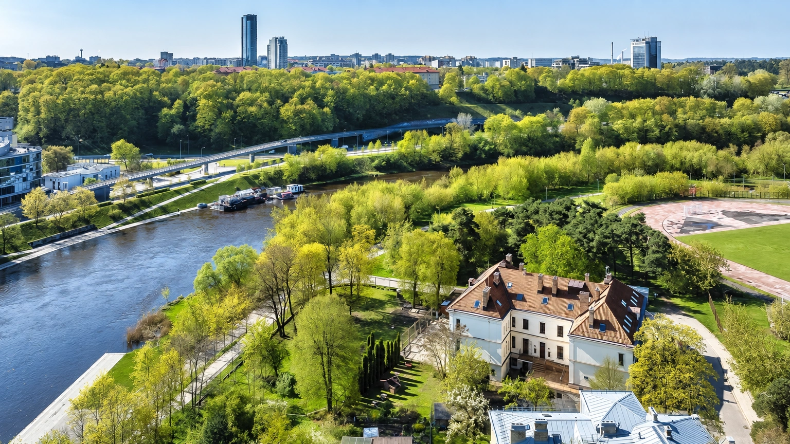 A building with a pitched roof among trees next to a river, seen from above.
